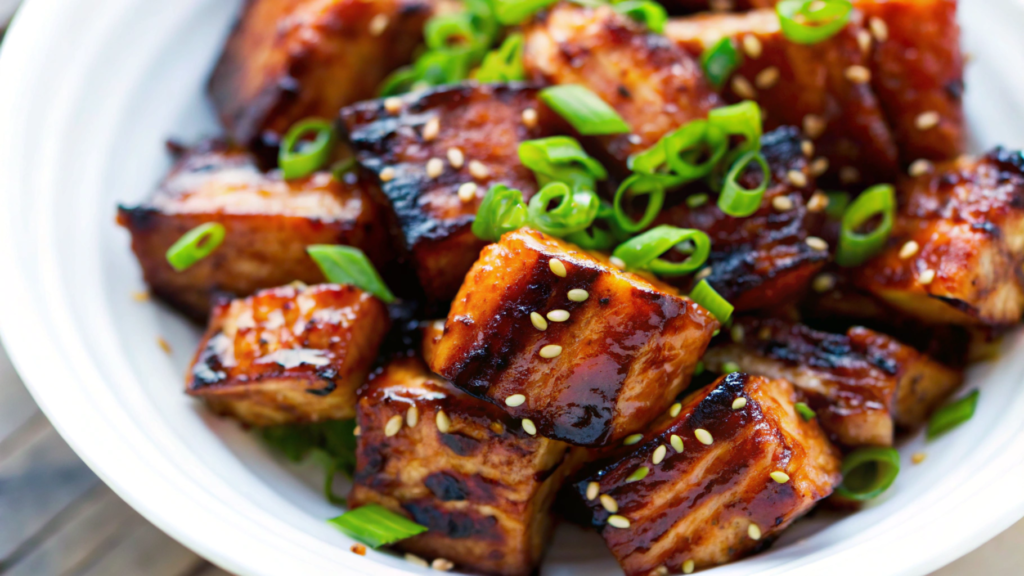 Bite-sized salmon cubes cooked to golden perfection, garnished with fresh herbs and lemon wedges on a white plate.